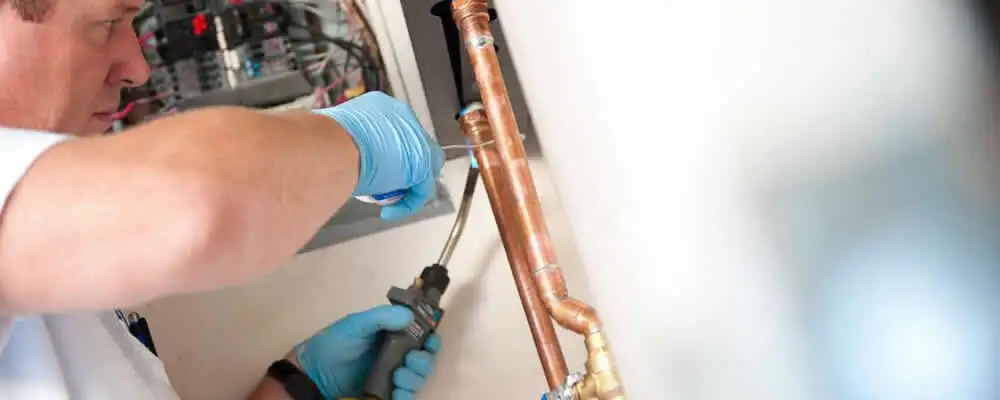 Water heater repair technician testing copper pipe connections and controls in Minneapolis, MN